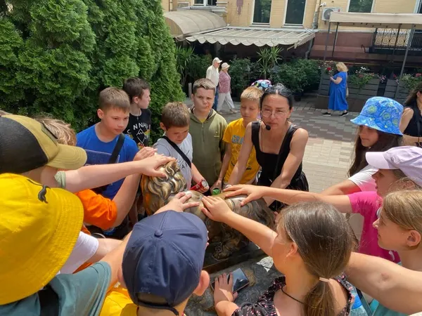 Школярі з гідом Jane торкаються бронзової скульптури під час квесту Загадай бажання в центрі Києва